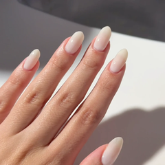 A close-up of a hand with long, almond-shaped nails painted in a glossy, pale cream or off-white shade.